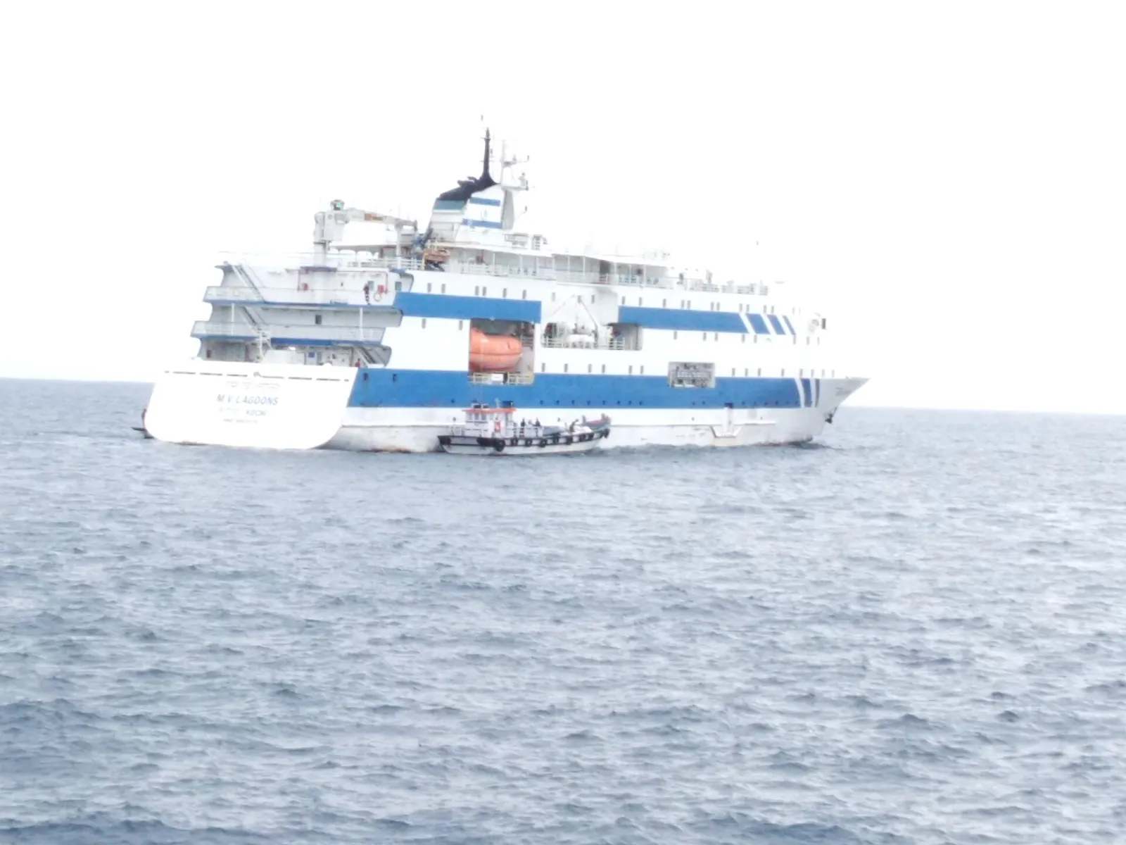 Blue-and-white passenger ship MV Lagoons at sea, with a small boat beside it